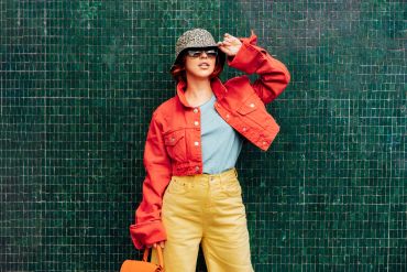 Fashionable woman posing in colorful outfit against green tiled wall.