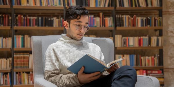 Young man reading a book in a cozy library chair.