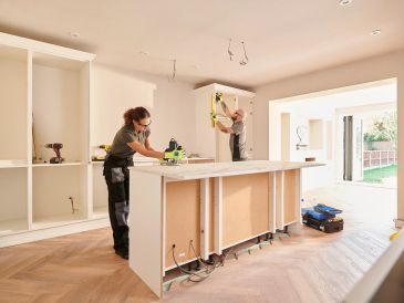 Two workers installing kitchen cabinets in a modern home.