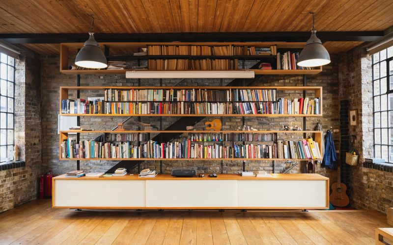 Stylish modern home interior with large book shelf laden with books in industrial style with wood floor and exposed brick walls