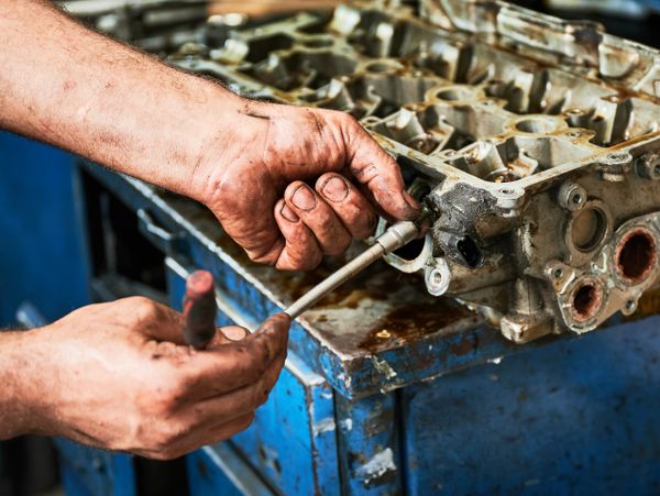 Mechanic working on a dirty engine part with tools.
