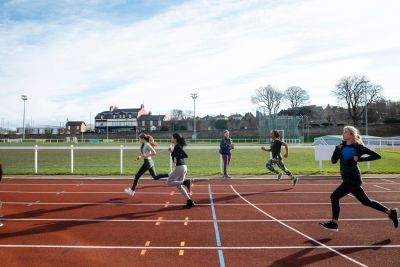 Four people running on an outdoor track during the day.