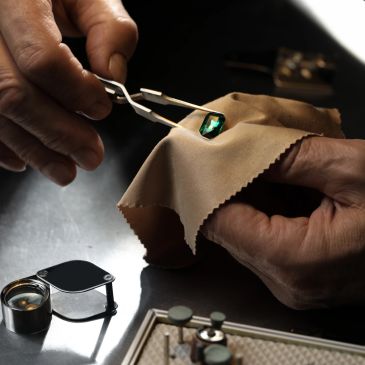 A jeweler carefully inspects a green gemstone with tweezers and a cloth.