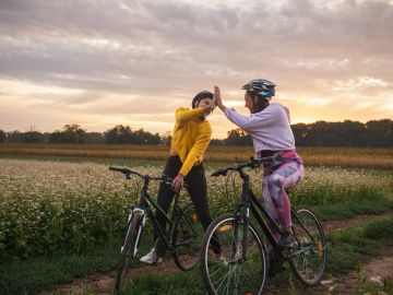 Two women biking and high-fiving in a field at sunset.