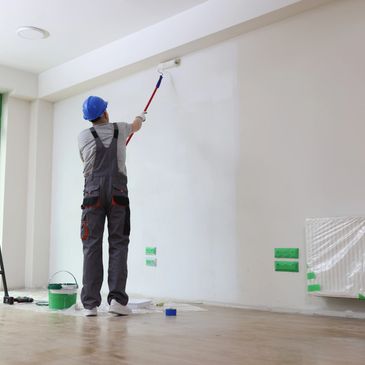 Worker painting a white wall with a roller indoors.