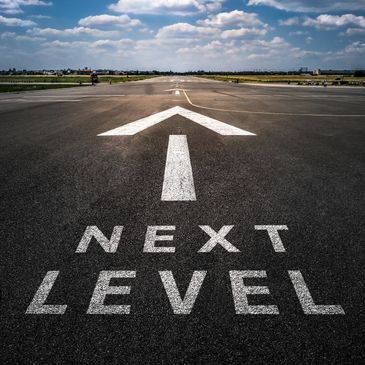 Runway with "NEXT LEVEL" and arrow painted, under a blue sky with clouds.