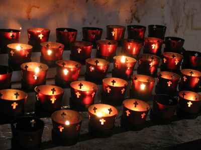 Lit votive candles in red holders with cross cutouts.
