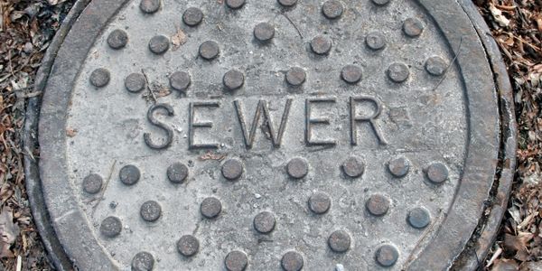 A round metal sewer manhole cover with textured dots and the word 'SEWER'.
