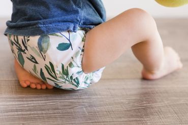 A baby wearing a leafy patterned diaper sitting on a wooden floor.