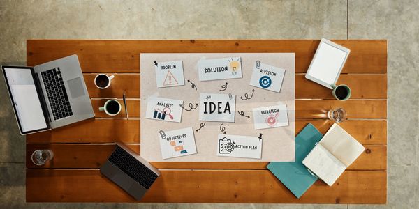 A wooden table with laptops, coffee, and a brainstorming idea chart.