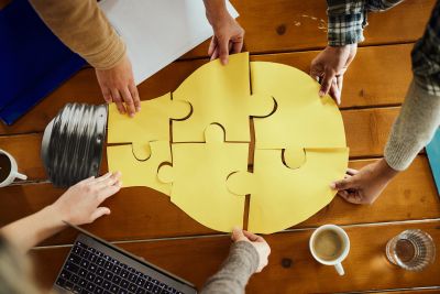 People assembling a light bulb puzzle symbolizing teamwork and ideas.