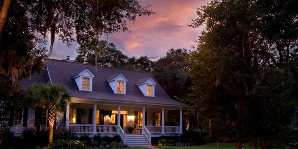 Cozy house with warm lights at sunset surrounded by lush greenery.