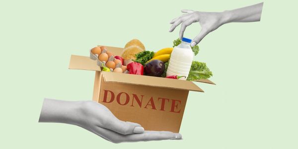 Hands exchanging a box labeled 'DONATE' filled with fresh groceries.