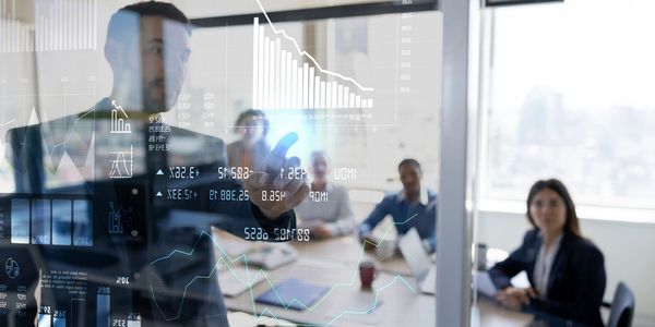 Man presenting financial data on a transparent screen to a team in a modern office.