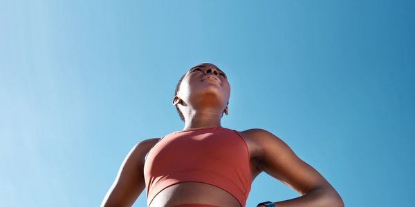 Woman in workout attire confidently looking up against a clear blue sky.