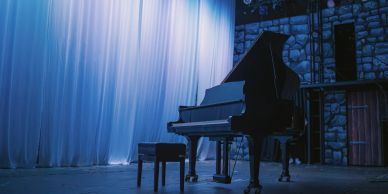 Grand piano and bench on stage with blue lighting.