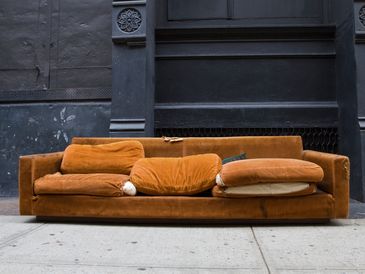Brown velvet sofa on a concrete sidewalk.