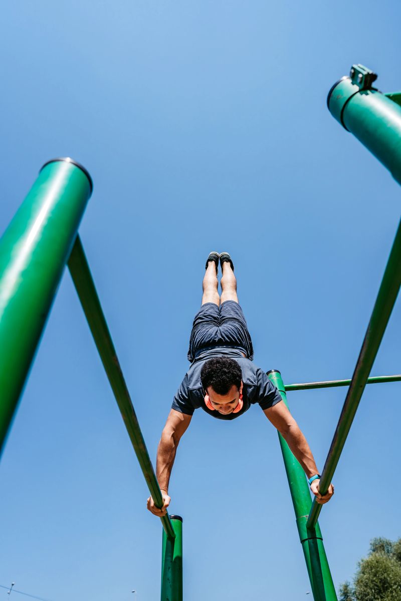 Handsome young mixed race man doing shoulder press exercises on the gym bars outdoors.