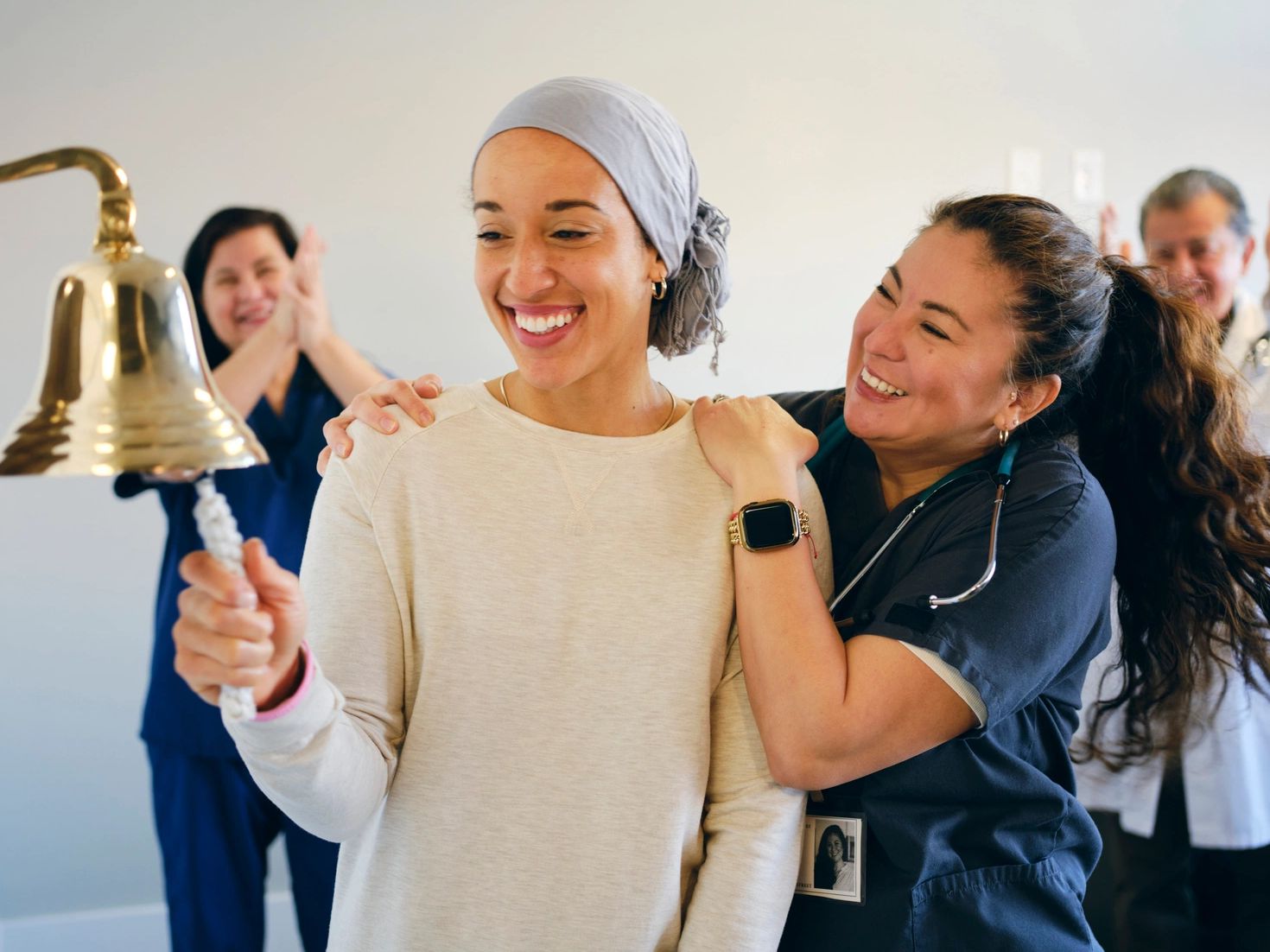 Woman rings bell in celebration with supportive healthcare workers around her.