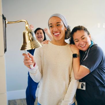 A woman rings a bell celebrating with happy nurses nearby.
