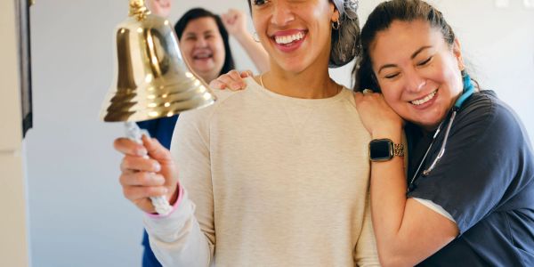 Healthcare worker rings bell, celebrating recovery with colleagues.