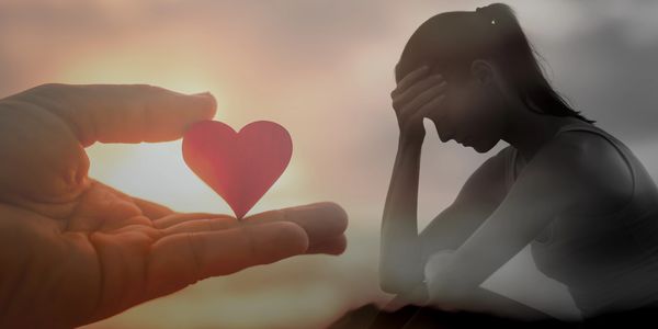 Hand holding a heart, woman upset in background.