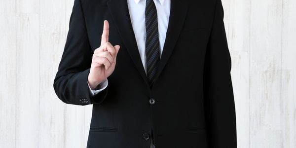 Man in black suit with raised index finger making a point.