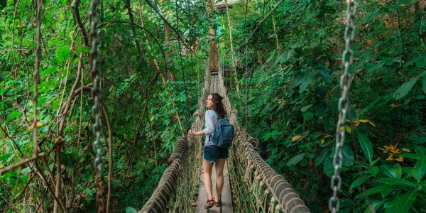 Woman with backpack crossing a rope bridge in dense forest.