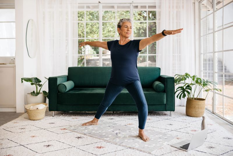 Mature woman showing her strength and flexibility as she practices the powerful warrior pose at home. Active senior woman doing yoga in an online fitness class, following a healthy workout routine.