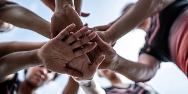 Group of people joining hands in a team huddle outdoors.