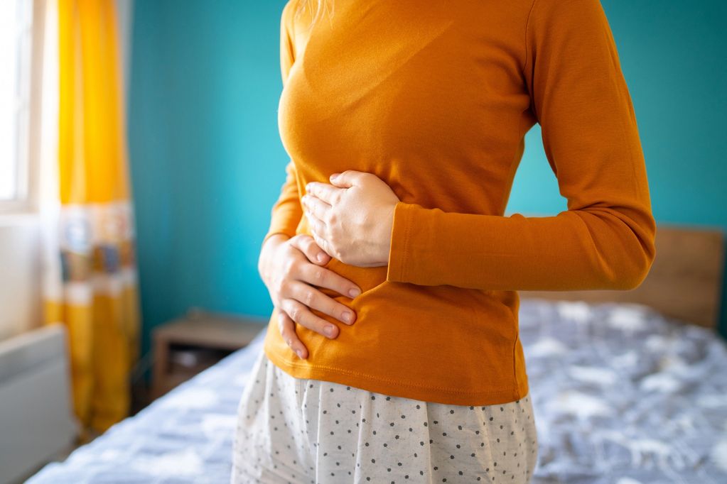 Karnını tutan turuncu üst giyen kadın.