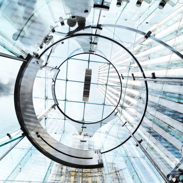 Looking up through a modern glass spiral staircase with metal railings.