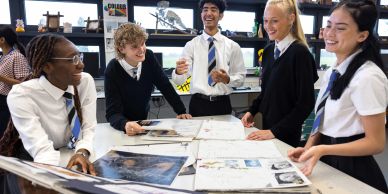 High school students collaborate around a table with art projects.