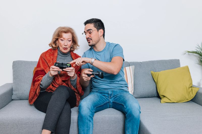 In this touching photograph, a mid-adult volunteer and an elderly woman sit together on a sofa, playing video games