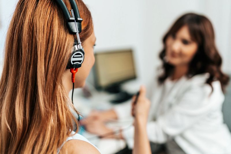 Audiologist doing impedance audiometry or diagnosis of hearing impairment. An beautiful redhead adult woman getting an auditory test at a hearing clinic.
