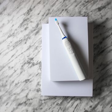 White electric toothbrush on white books on marble surface.