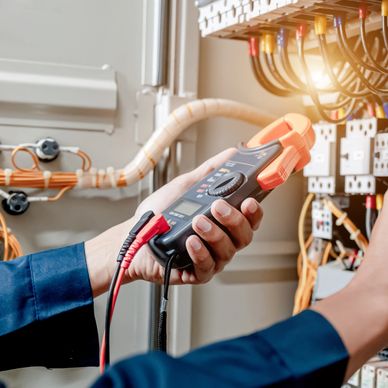 Technician testing electrical circuits with a multimeter in a control panel.