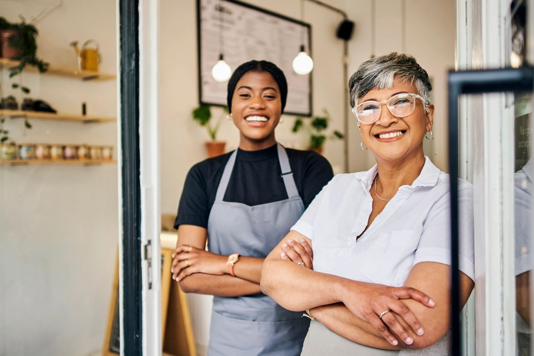 Two smiling women standing confidently at a cafe entrance.