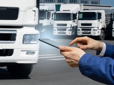 Person using a tablet for telematics report near parked white trucks in a logistics yard.