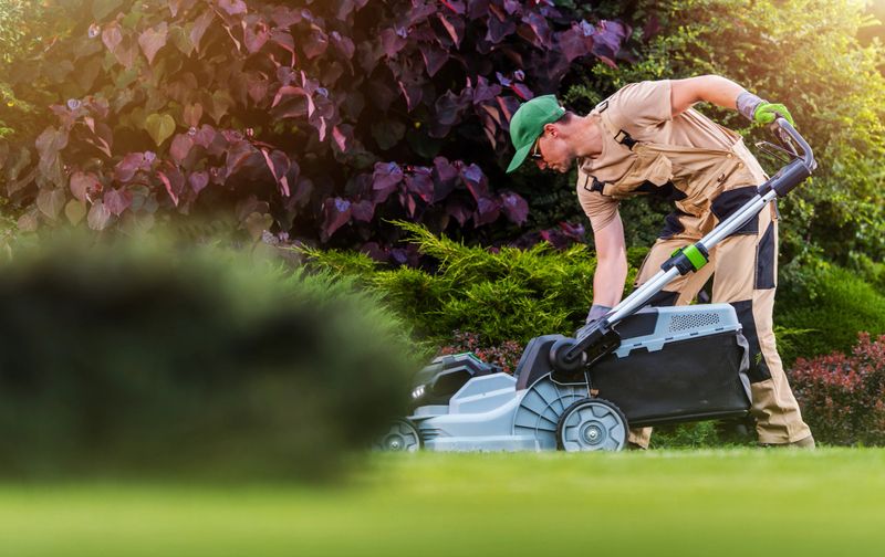 Caucasian Garden and Landscaping Worker Mowing  Backyard Lawn Using Electric Cordless Grass Mower. Garden Maintenance Theme.