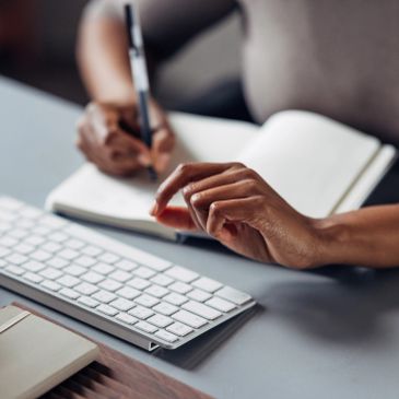 Person writing in a notebook near a keyboard.