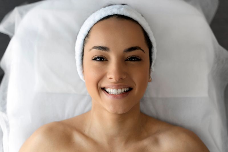 Top view of smiling woman laying at the couch after making an effective facial procedure. Lady looking at the camera. Stock photo