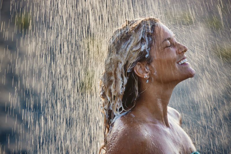 Happy woman enjoying while washing her hair under the shower outdoors. Copy space.