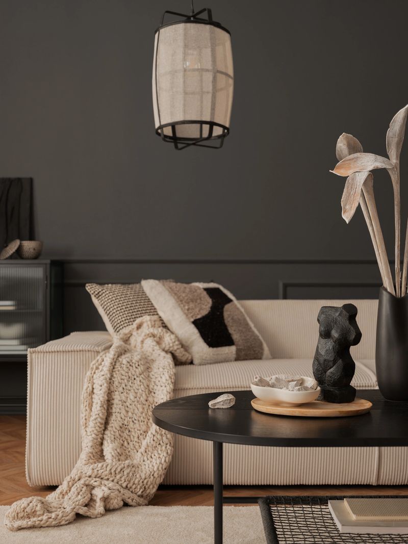 Interior design of elegant living room with modular sofa, patterned pillows, plaid, vase with dried flowers, lamp, sculpture, bowl, books, dark wall and personal accessories. Home decor. Template.