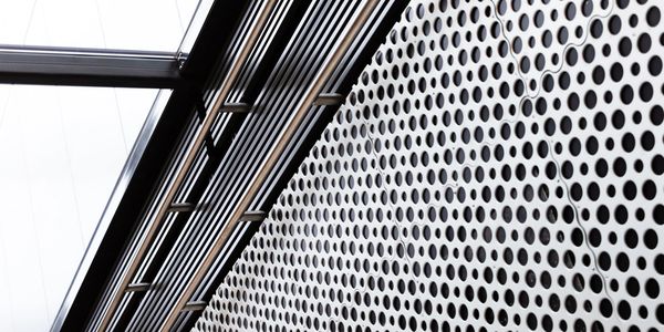 Close-up of a perforated metal wall with pipes and beams above.