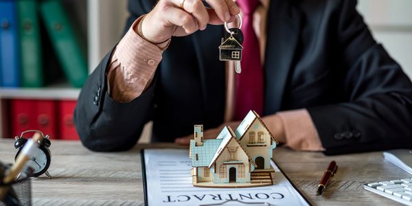 Pessoa segurando chave de casa acima de contrato imobiliário.