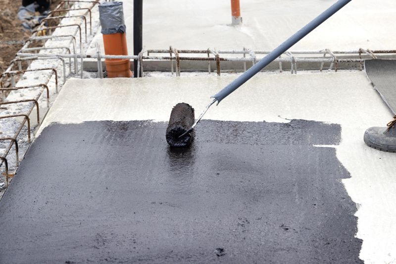 Worker applying a bituminous primer on a concrete slab at a construction site before laying bituminous waterproofing