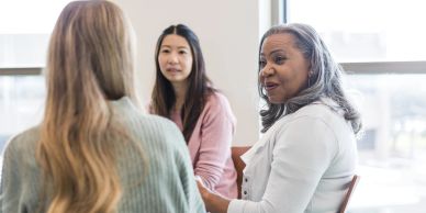 Three women engaged in a serious conversation indoors.