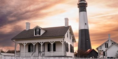 Lighthouse and adjacent white houses with a white picket fence at sunset.