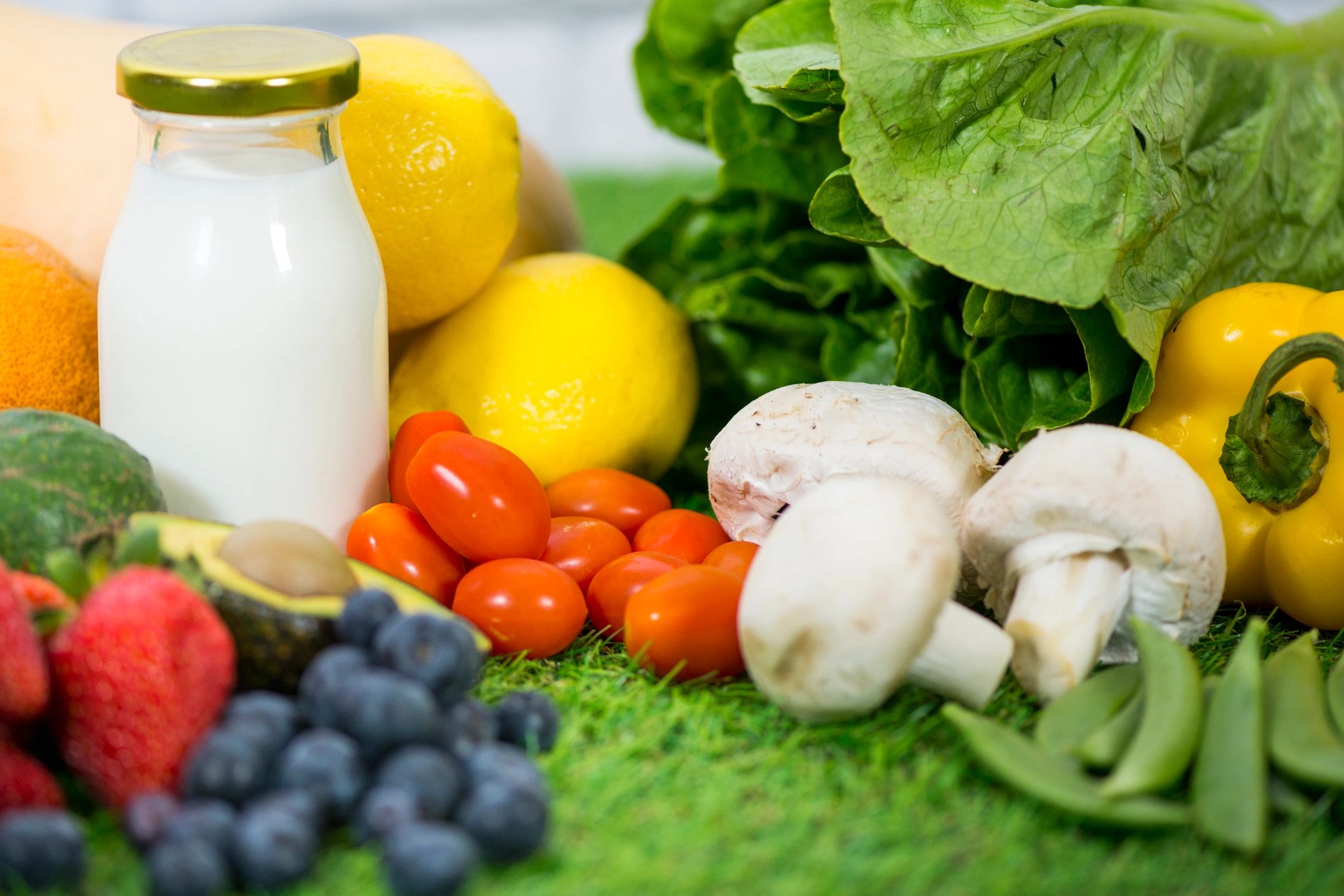 Fresh fruits, vegetables, and a bottle of milk on a green surface.